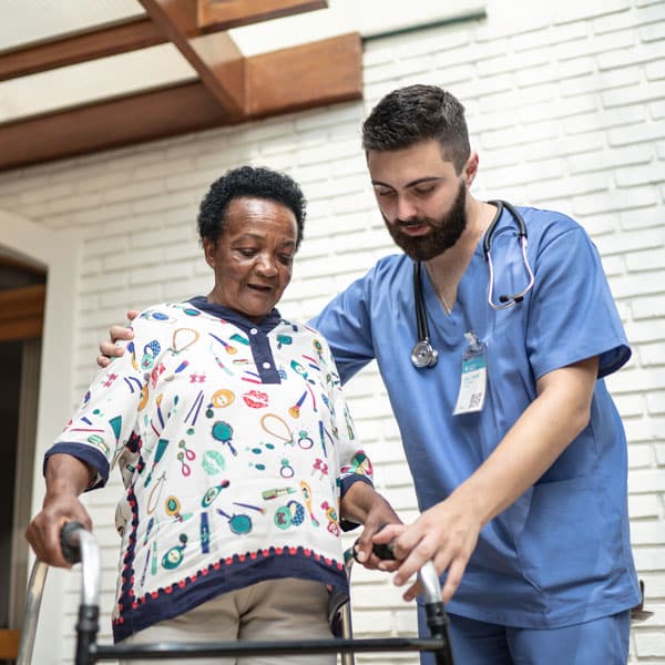 male caregiver helping a senior woman using a walker leave her home